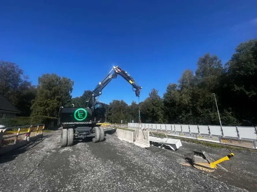 Svart hjulgrävare med Leons-logotyp lyfter betongelement vid en väg