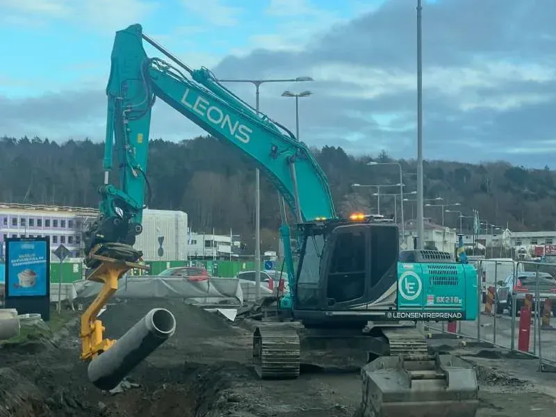 Grävmaskin med Leons-dekor som lyfter ett betongrör