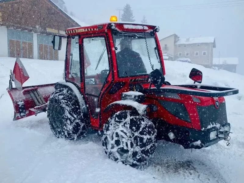 Röd traktor med snöplog och snökedjor i snöfall